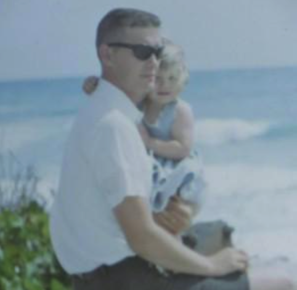 Dad holding me on his lap with the sea in the background.